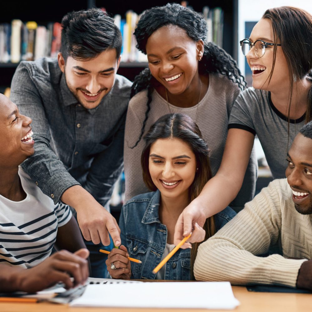 Students laughing in library, studying together for exam or research for project, education and teamwork. Diversity, funny and young men with women in study group, learn together and happy on campus.